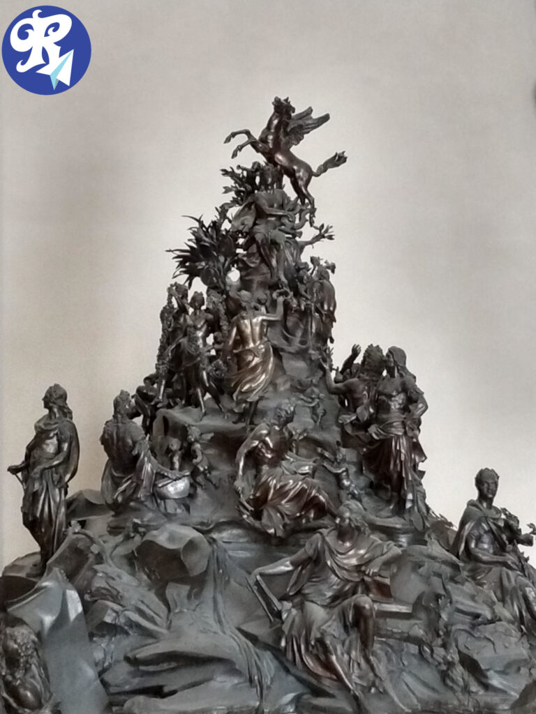 Le Parnasse Français, de Louis Garnier, Simon Curé, Augustin Pajou - Grupo, Bronze e Madeira, 1.718-1.762. A imagem mostra uma escultura detalhada e intricada com várias figuras arranjadas em uma estrutura rochosa e montanhosa. No topo da escultura, há um cavalo alado, Pégaso, cercado por várias figuras humanas em poses dinâmicas. As figuras parecem estar engajadas em diferentes atividades, com algumas segurando objetos como pergaminhos ou ferramentas. A escultura é altamente detalhada, com roupas esvoaçantes e posturas expressivas, sugerindo uma cena de importância mitológica ou histórica. A habilidade e a complexidade da escultura fazem dela uma peça de arte interessante e relevante. Contém os seguintes integrantes: 1, Pégaso 2, Louis XIV - Como APolo 3, As Três Graças: Antoinette Des Houlières, Henriette de La Suze e Madeleine de Scydéry 4, Pierre Corneille 5, Jean Racine 6, Jean-Baptiste Poquelin, dit Molière 7, Claude-Emmanuel Luillier, dit Chapelle 8, François-Marie Arouet, dit Voltaire 9, Jean-Baptiste Rousseau 10, Prosper Jolyot de Crébillon 11, Evrard Titon du Tillet As figuras estão no topo e vão descendo de acordo com a numeração.